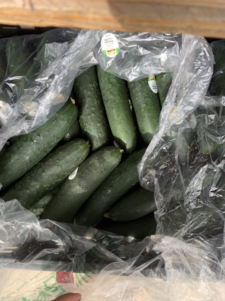 A pile of fresh, dark green cucumbers with small stickers inside a partially open plastic bag on a wooden surface.