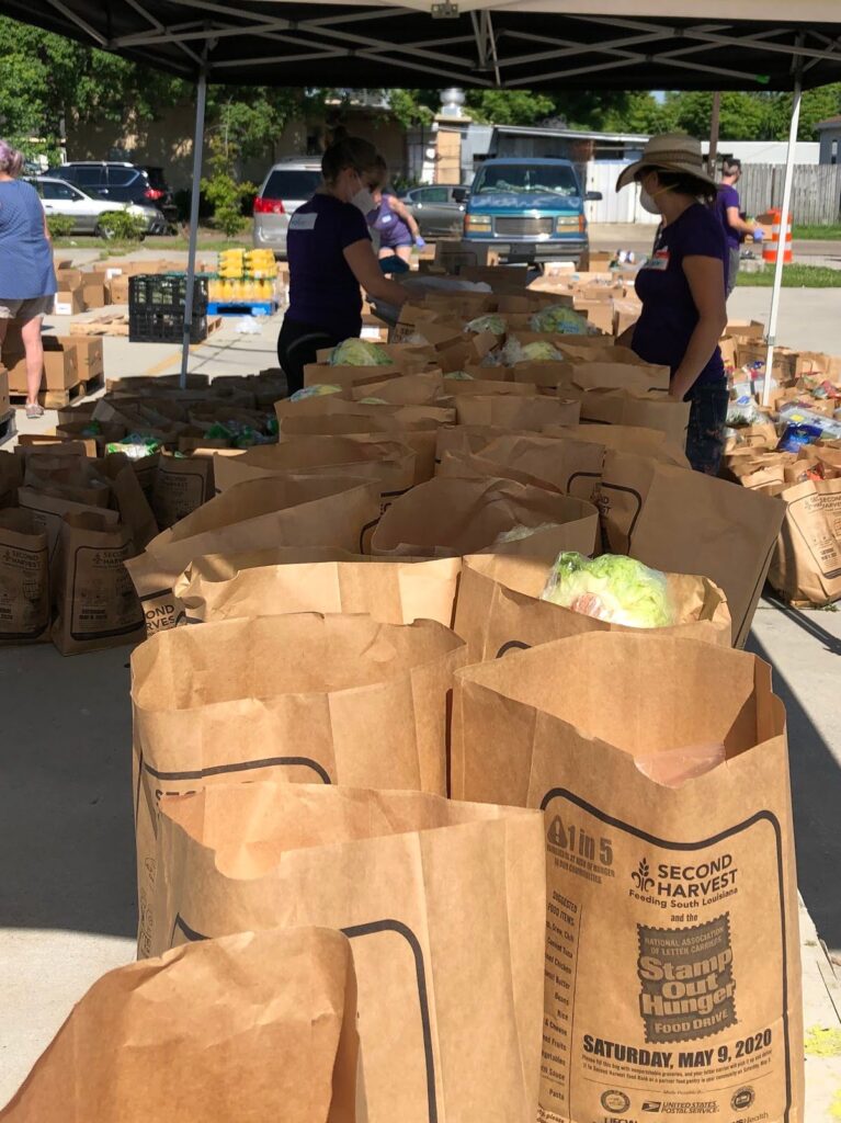 Volunteers organize brown paper bags filled with groceries under a tent at a food drive.