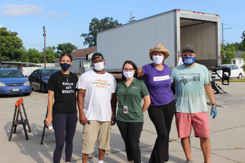Five people wearing masks stand arm-in-arm in front of a truck outdoors, smiling.